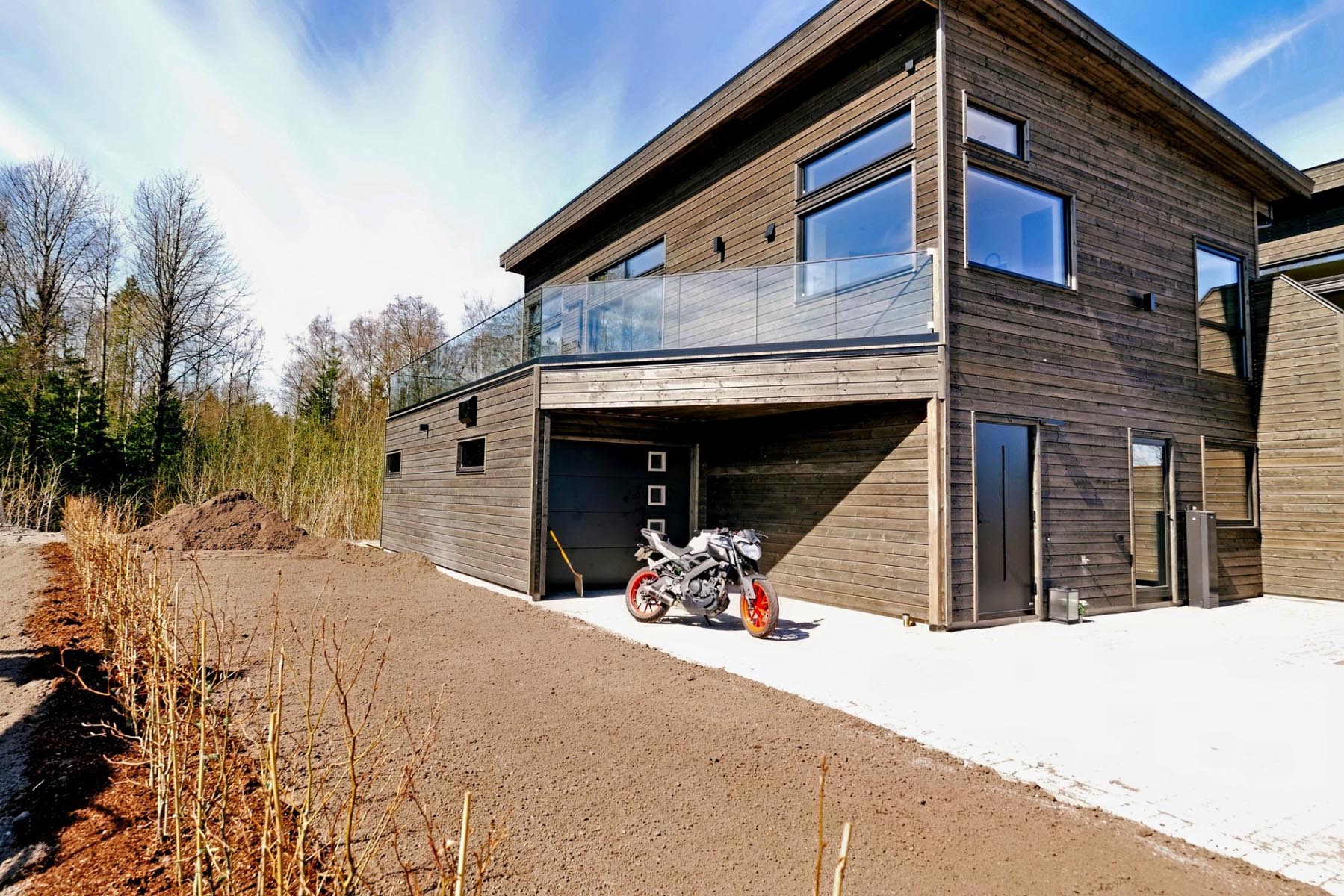 Et nybygd moderne hus fra utsiden med mørke treplanker og store vinduer.